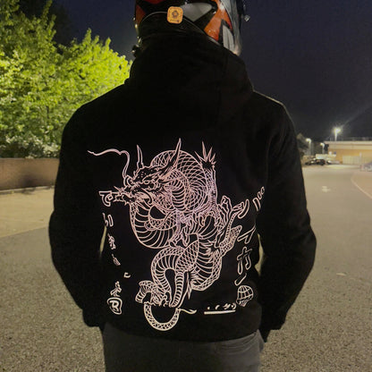 Person wearing a black hoodie with a dragon design on the back, standing in an outdoor setting at night.